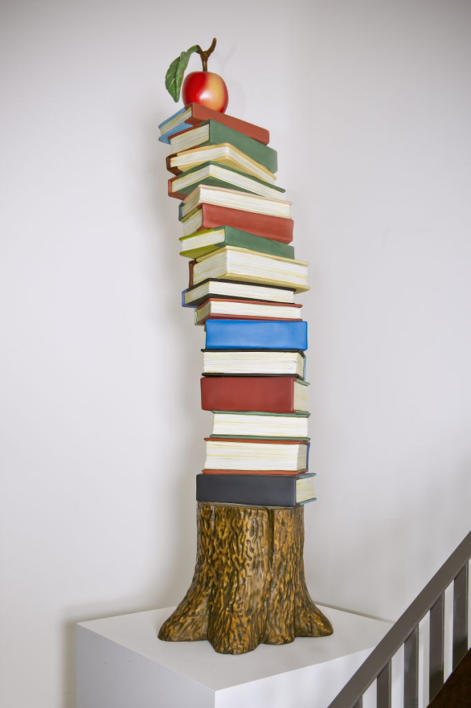Books stacked on top of a tree stump with an apple on the top