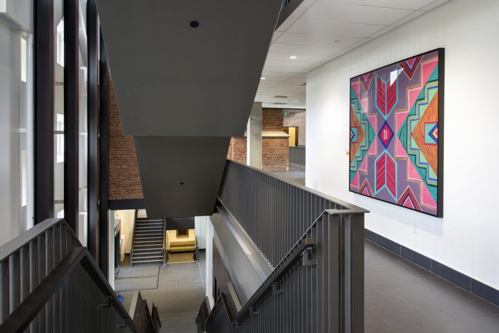 View of a brightly-patterned abstract painting in a hallway, next to a stairwell