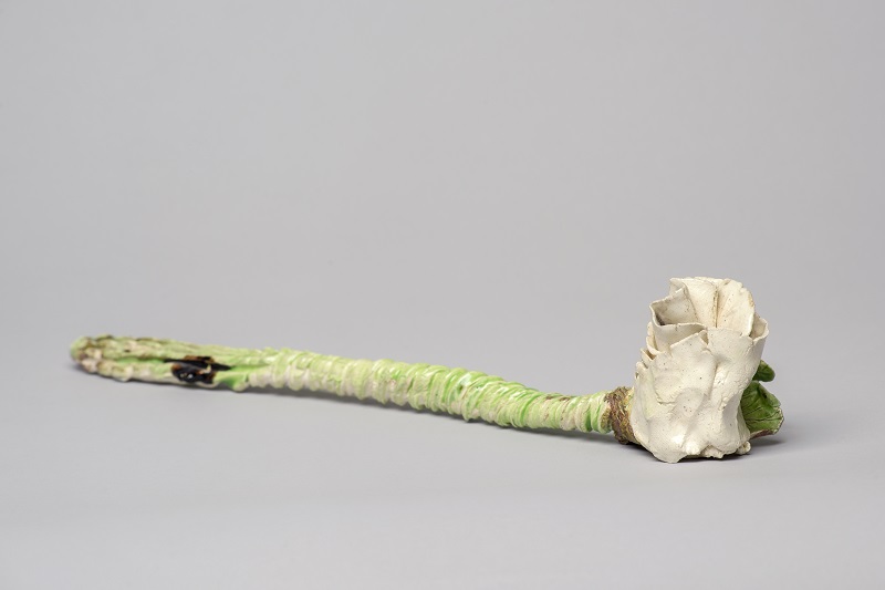 A glazed, long-stemmed white ceramic rose with a textured, light green stem