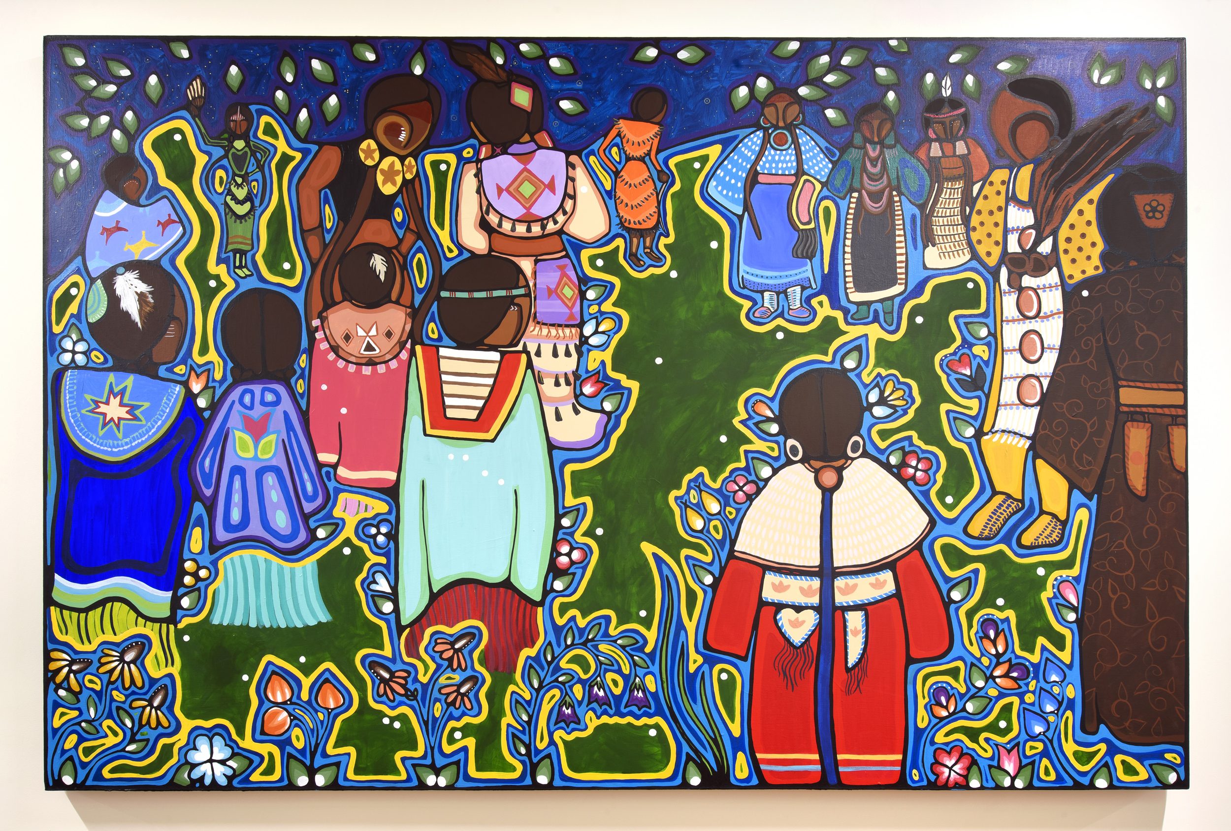Image depicting a large group of women at a powwow in brightly patterned, traditional regalia. Predominant colours are green blue, red, and yellow