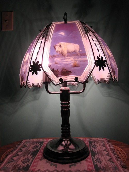 Photograph of a lit lamp on a woven mat. The lamp has an image of a white bison in a purple, snowy landscape.